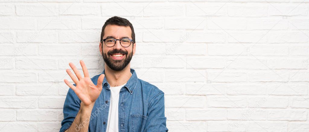 Handsome man with beard over white brick wall counting five with fingers