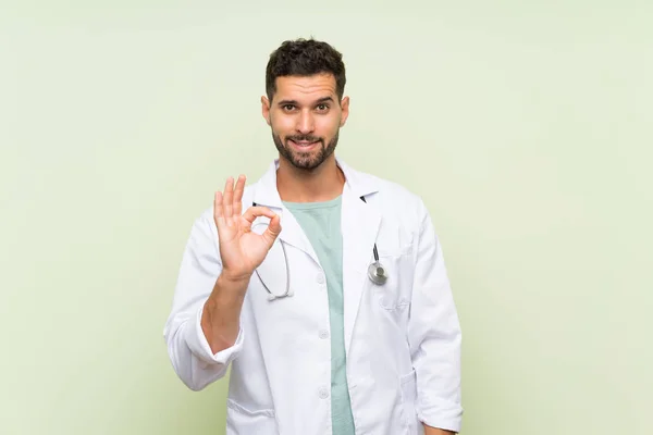 Młody Lekarz Człowiek Nad Odizolowaną Zieloną Ścianę Pokazując Znak Palcami — Zdjęcie stockowe