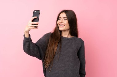 Soyutlanmış pembe arka planı olan genç bir kadın selfie çekiyor.