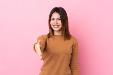 Soyutlanmış pembe arka planda genç bir kadın iyi bir anlaşma için el sıkışıyor.