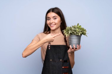 İzole edilmiş mavi arka planda genç bir kadın bir saksı alıp ona doğrultuyor.