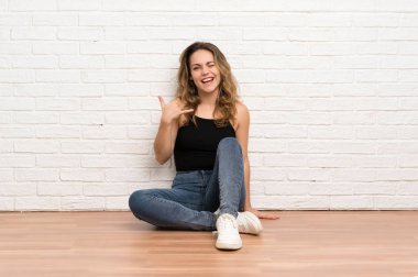 Genç sarışın kadın telefon jesti yaparak katta oturuyor