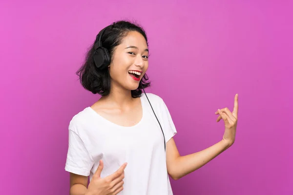 Asiática joven escuchando música con un móvil y bailando sobre aislada pared púrpura — Foto de Stock