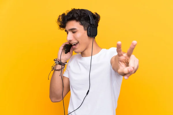 Jovem argentino ouvindo música com um celular sobre uma parede amarela isolada — Fotografia de Stock