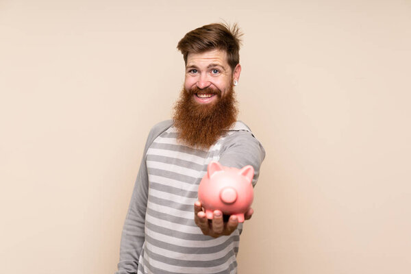 Redhead man with long beard over isolated background holding a big piggybank