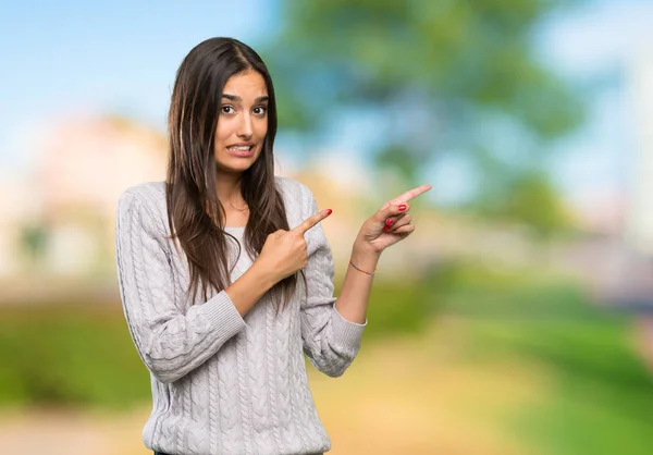 Young hispanic brunette woman frightened and pointing to the side at outdoors