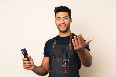 Kuaför veya berber elbisesi ile izole arka plan üzerinde genç yakışıklı adam ve saç kesme makinesi tutarak