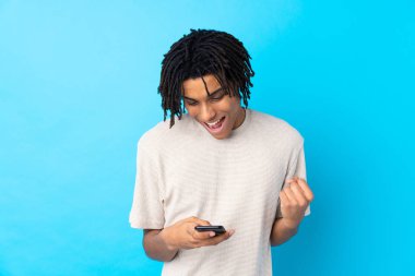 Genç Afrikalı Amerikalı bir adam mavi arka planda şaşırdı ve bir mesaj gönderiyor.