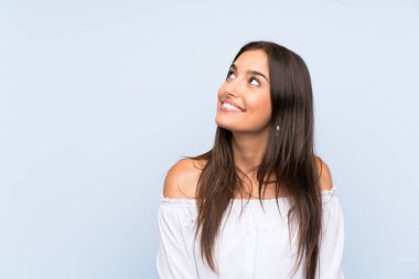 Izole mavi arka plan üzerinde genç kadın gülüyor ve yukarı bakıyor