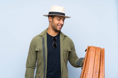 Genç yakışıklı bir adam, izole edilmiş mavi arka planda, mutlu bir ifadeyle antika bir evrak çantası tutuyor.