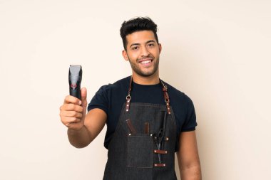 Kuaför veya berber elbisesi ile izole arka plan üzerinde genç yakışıklı adam ve saç kesme makinesi tutarak