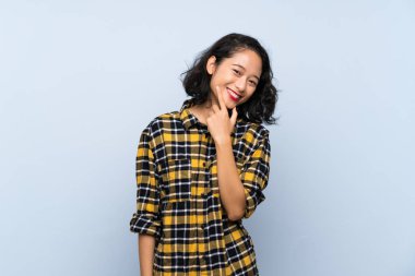 Asyalı genç bir kadın mavi arka planda sırıtıyor.