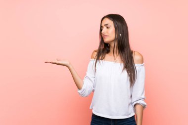 İzole edilmiş pembe arka plan üzerinde genç bir kadın kopyalama alanını kuşkularla dolduruyor