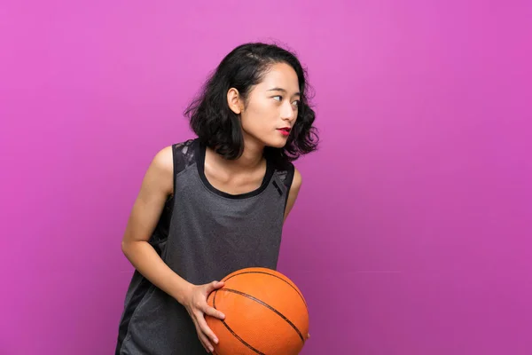 Giovane donna asiatica che gioca a basket su sfondo viola isolato — Foto Stock