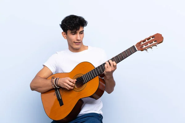 Jovem argentino com guitarra sobre fundo azul isolado — Fotografia de Stock