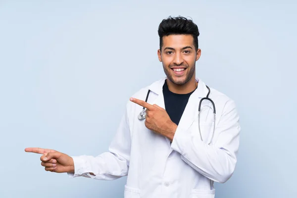 Jovem Médico Homem Sobre Isolado Parede Azul Surpreendido Apontando Lado — Fotografia de Stock