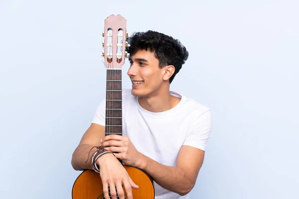 Jonge Argentijnse man met gitaar over geïsoleerde blauwe achtergrond — Stockfoto