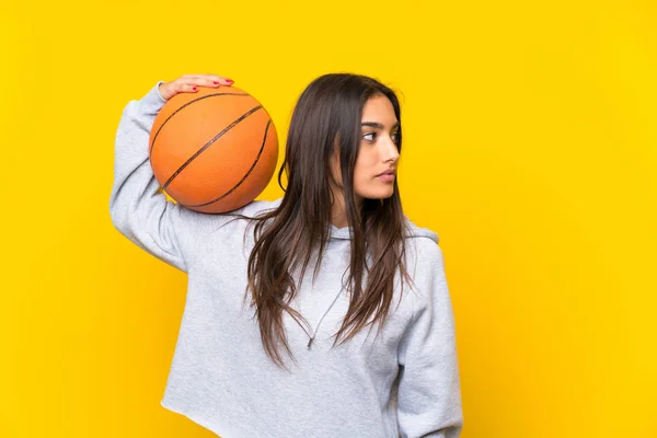 Молодая женщина играет в баскетбол на изолированном желтом фоне — стоковое фото
