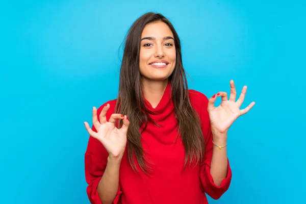 Young woman with red sweater over isolated blue background showing an ok sign with fingers