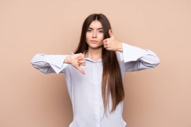Izole arka plan üzerinde genç bir kadın iyi-kötü işareti yapıyor. Evet ya da değil arasında kararsız