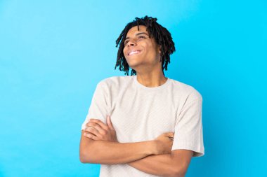 Genç Afro-Amerikalı adam mavi arka planda, gülümserken yukarı bakıyor.