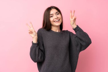 Soyutlanmış pembe arka planda genç bir kadın zafer işaretini iki eliyle gösteriyor.