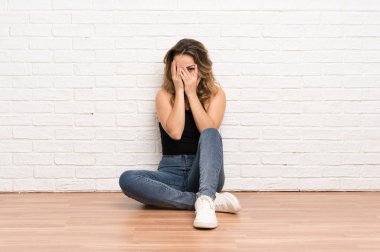 Genç sarışın kadın gözleri kaplayan ve parmaklardan bakarak katta oturan