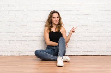 Genç sarışın kadın yan parmak işaret yerde oturan