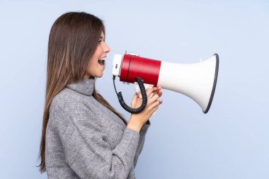 İzole edilmiş mavi arka planda genç Brezilyalı kız megafondan bağırıyor.