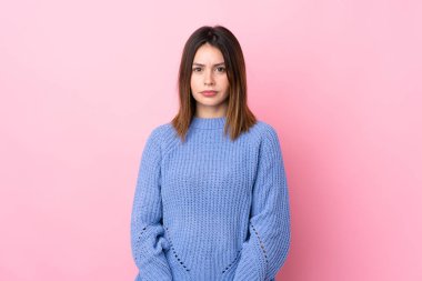 İzole edilmiş pembe arka planda mavi kazaklı genç kadın üzgün.