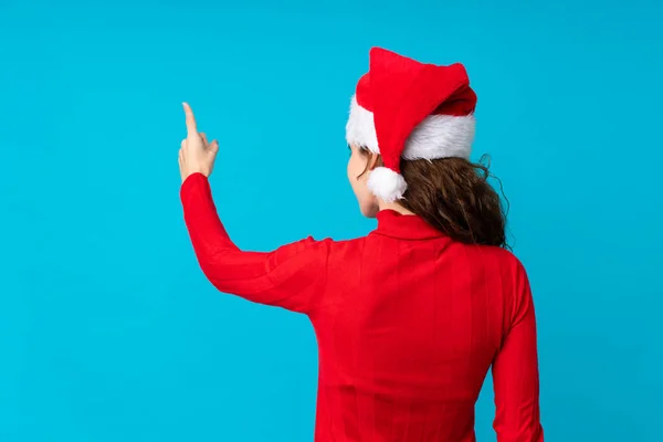 头戴圣诞礼帽 背对孤立的黄色背景 用食指指向后的女孩 — 图库照片