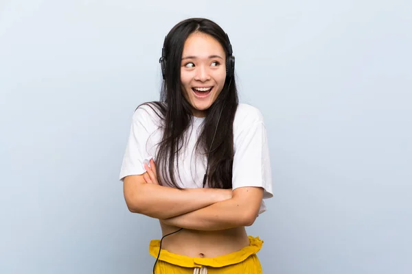 Tinédzser ázsiai lány hallgat zenét át elszigetelt kék fal énekel — Stock Fotó