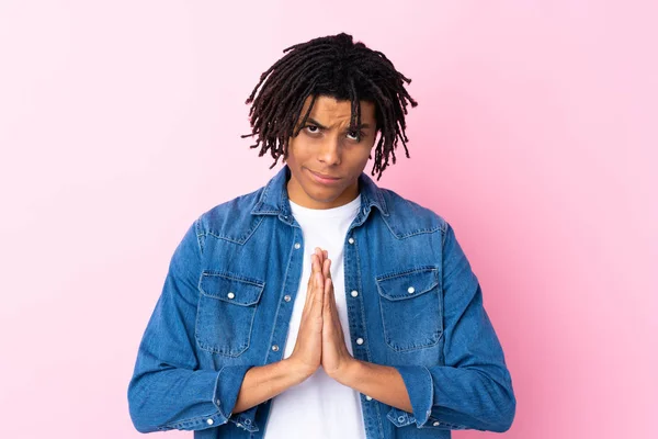 Young African American man with jean shirt over isolated pink background pleading