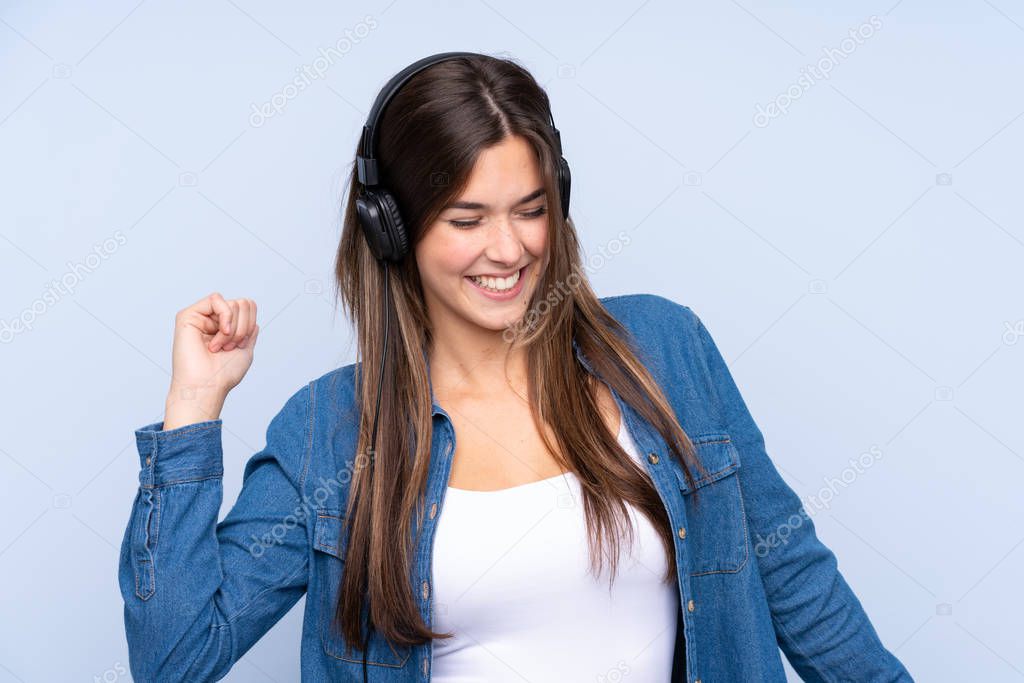 Teenager Brazilian girl listening music and dancing over isolated blue background