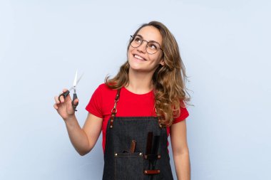 Kuaför ya da berber elbiseli genç sarışın kadın yukarı bakıyor.