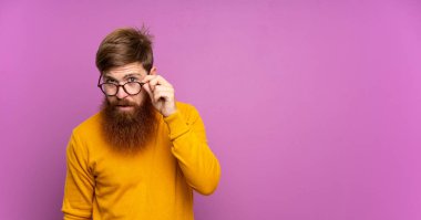 Kızıl saçlı, uzun sakallı, gözlüklü ve mutlu mor bir geçmişi olan bir adam.