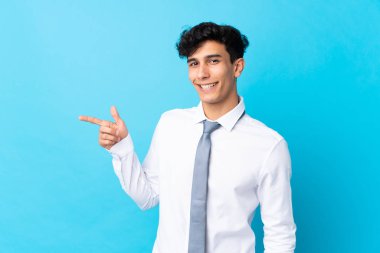 Arjantinli genç işadamı, izole edilmiş mavi arka planda parmağını kenarı işaret ediyor.