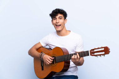 Gitarlı genç Arjantinli adam mavi arka planda zaferi kutluyor.