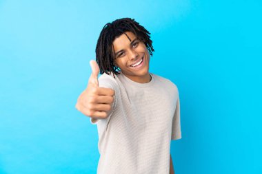 Genç Afro-Amerikalı adam mavi arka planda. Başparmakları havada. Çünkü iyi bir şey oldu.