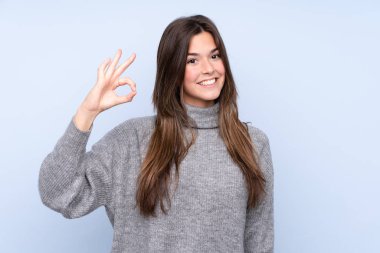 İzole edilmiş mavi arka plan üzerinde Brezilyalı genç bir kız parmaklarıyla tamam işareti gösteriyor
