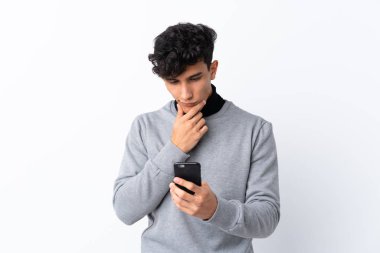 Arjantinli genç adam izole edilmiş beyaz bir arka plan düşünüyor ve mesaj gönderiyor.