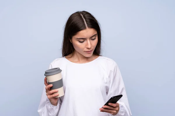 Giovane Donna Sfondo Blu Isolato Possesso Caffè Portare Cellulare — Foto Stock