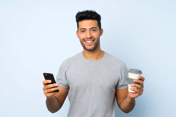 年轻的帅哥在孤立的背景拿着咖啡带走和手机 — 图库照片