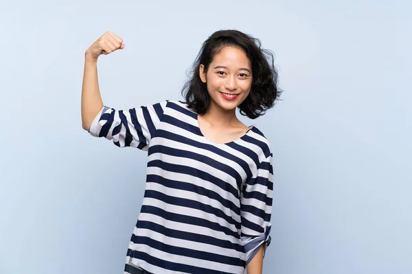 亚洲年轻女子在孤独的蓝色背景上做着强有力的手势 — 图库照片