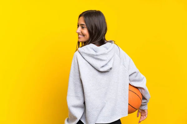Wanita muda bermain basket melalui latar belakang kuning yang terisolasi — Stok Foto