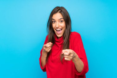 İzole edilmiş mavi arka plan üzerinde kırmızı süveterli genç bir kadın sana işaret ediyor.