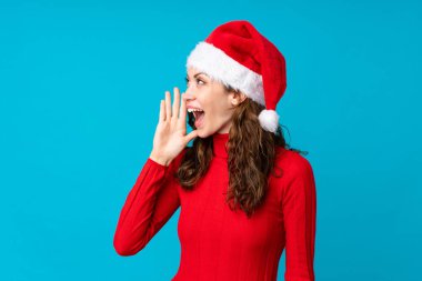 İzole edilmiş sarı arka planda Noel şapkalı kız ağzı açık bağırıyor.