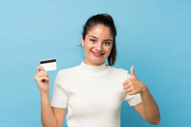 Genç esmer kız izole edilmiş mavi arka planda elinde bir kredi kartıyla