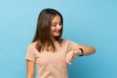 Kol saatine bakarak izole edilmiş mavi arka planda esmer bir kız.