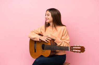 Gitarlı, pembe arka planlı, esmer genç bir kız.